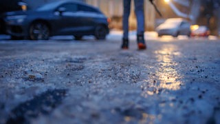 Eis glitzert am frühen Morgen auf einem Gehweg: In Rheinland-Pfalz kann es glatt werden (Symbolbild)