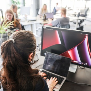 Auch in RLP tobt eine Debatte um den CDU-Vorschlag zur Teilzeit - In einem Großraumbüro arbeitet eine Frau an Laptop und Monitor (Symbol) 