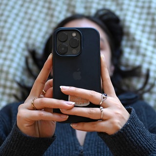 Eine junge Frau liegt mit dem Smartphone in der Hand auf dem Bett.