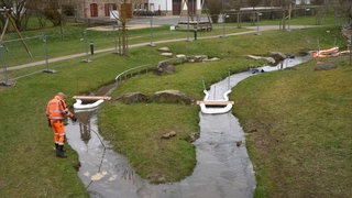 Mit einer Ölsperre pumpen Arbeiter mit Diesel kontaminiertes Oberflächenwasser aus einem Bach ab, der in der in Kisselbach an einem Spielplatz vorbeifließt