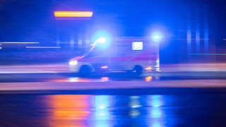 Ein Krankenwagen fährt im Dunkeln mit Blaulicht auf einer Straße. Bei Frankenthal ist ein Autofahrer nach einem Überholmanöver gestorben.