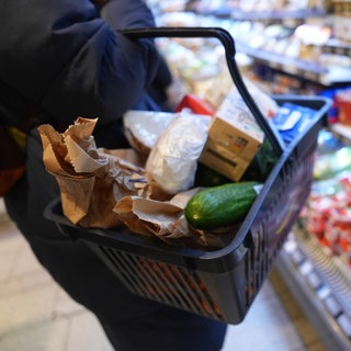 Eine Kundin geht mit einem Einkaufskorb und ihrem Einkauf an den Regalen in einem Supermarkt vorbei.