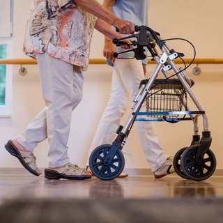 Eine Pflegekraft geht in einem Pflegeheim mit einer älteren Frau über einen Korridor. Die Pflegekammer RLP hat ihre umstrittene Mitgliederbefragung gestoppt.