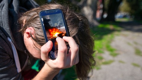 Ein verzweifelter Mann mit einem Handy, auf dem Kriegsszenen zu sehen sind. Was machen Krisen mit unserer Psyche?