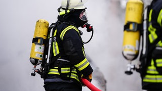 Feuerwehrmann mit Schlauch (Symbolfoto)  Raetselhafte Brände und Auto in Flemmen auf A3