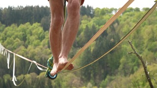 Mensch steht Barfuß auf einer Slackline