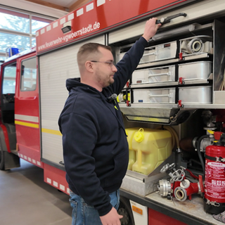 Christian vor einem Feuerwehrauto. Er engagiert sich ehrenamtlich bei der Freiwilligen Feuerwehr in Vendersheim.