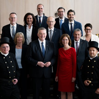 Gruppenfoto der RLP-Regierung mit den 10 Ministern und Ministerinnen, Ministerpräsident Gordon Schnieder und zwei Schornsteinfegern.