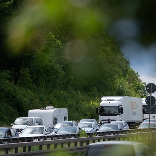 Autos stehen auf einer Autobahn hinter einer Leitplanke im Stau an einem Pfingstwochenende.