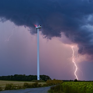 ein blitz zuckt senkrecht am Himmel bis zum Boden, in der Nähe steht ein Windrad