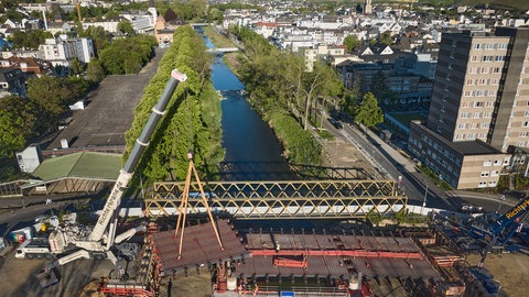 Kräne heben den letzten Teil der neu errichteten Landgrafenbrücke in Bad Neuenahr-Ahrweiler in ihre Position (Aufnahme mit einer Drohne). Die alte Brücke wurde durch die Flutkatastrophe 2021 total zerstört.