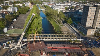 Kräne heben den letzten Teil der neu errichteten Landgrafenbrücke in Bad Neuenahr-Ahrweiler in ihre Position (Aufnahme mit einer Drohne). Die alte Brücke wurde durch die Flutkatastrophe 2021 total zerstört.