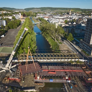Kräne heben den letzten Teil der neu errichteten Landgrafenbrücke in Bad Neuenahr-Ahrweiler in ihre Position (Aufnahme mit einer Drohne). Die alte Brücke wurde durch die Flutkatastrophe 2021 total zerstört.