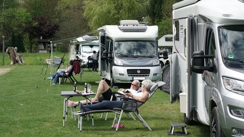 Zwei Camper liegen vor ihrem Wohnmobil in der Sonne