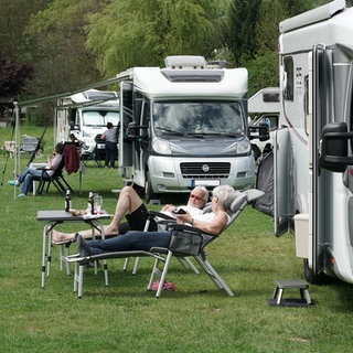 Zwei Camper liegen vor ihrem Wohnmobil in der Sonne
