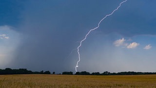 Ein Blitz leuchtet vor dunklen Gewitterwolken (Symbolbild) - nach der Hitze kommen Gewitter nach RLP