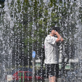 Wegen Hitze: Ein Mann steht in kurzer Hose und T-Short zur Abkühlung mitten in einem Springbrunnen.