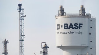 Ein Turm mit der Aufschrift "BASF" steht neben Schornsteinen auf dem Werksgelände des Chemiekonzerns BASF. Der Konzern muss sparen und will sich neu aufstellen.