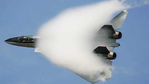 Ein Kampfjet fliegt mit Überschallgeschwindigkeit und durchbricht gerade die Schallmauer.