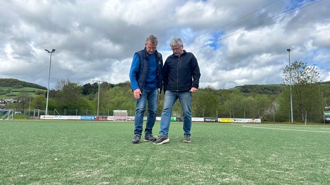 Bürgermeister und Vorsitzender stehen auf dem Kunstrasen und kontrollieren diesen auf mögliche Schäden.