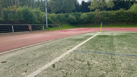 Rand eines sehr sandigen Fußballfeldes mit angrenzender Laufbahn.