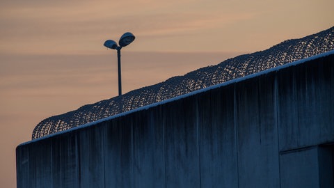 Die dicke Mauer eines Gefängnisses mit Stacheldraht.