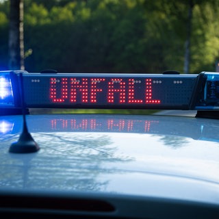 Ein Einsatzfahrzeug, Streifenwagen, der Polizei steht mit Blaulicht und dem Schriftzug Unfall im Display an einem Unfallort.