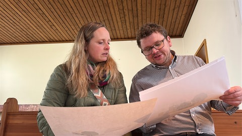 Lukas und Lara Schur wollen direkt hinter der Kirche auch ein Wohnhaus bauen. Auf dem ehemaligen Altar des Gotteshauses begutachten sie die Pläne dazu.