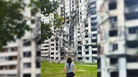 Daria Lunina steht vor einem zerstörten Haus bei ihrem Besuch in Charkiw 2023
