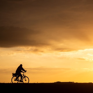 Ein Fahrradfahrer fährt bei Sonnenaufgang über einen Feldweg.