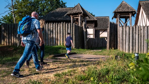 Ein Mann und ein Junge auf dem Weg ins Keltendorf in Steinbach im Donnersbergkreis. Sie gehen gerade durch das hölzerne Eingangstor. 
