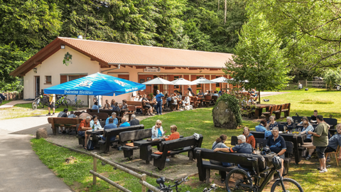 Viele Wanderer sitzen auf Bänken im Sonnenschein vor der Gräfensteinhütte in Merzalben in der Südwestpfalz.