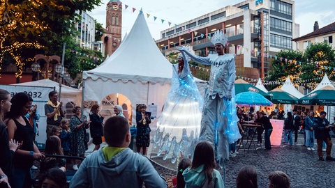 2 Stelzenläufer in hellblauem LED-Gewand präsentieren sich auf dem Festplatz des Schlabbeflicker-Festivals in Pirmasens