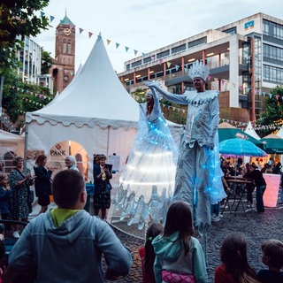 2 Stelzenläufer in hellblauem LED-Gewand präsentieren sich auf dem Festplatz des Schlabbeflicker-Festivals in Pirmasens