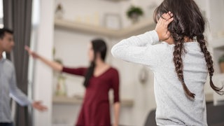 Wenn sich Eltern nach der Scheidung oder Trennung uneins sind, mit welchem Elternteil das Kind mehr Zeit verbringen sollte, hilft das Team vom Kaiserslauterer Kinderschutzbung "Begleiteten Umgang". (Mädchen steht vor ihren streitenden Eltern und ist traurig.)