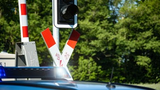 Ein Streifenwagen der Polizei steht mit Blaulicht vor einem beschrankten Bahnübergang. 