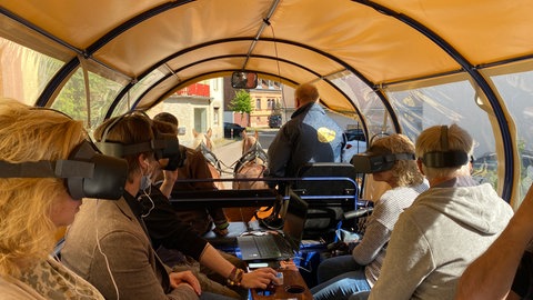 Teilnehmer der virtuellen Zeitreise durch Otterberg sitzen auf einem Planwagen, der von Pferden gezogen wird.