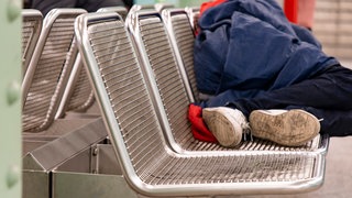 Ein Obdachloser schläft auf Bänken an einem Bahnhof. So wurde jetzt ein Obdachloser in Kaiserslautern angegriffen.