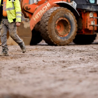 Ein Bagger und ein Arbeiter auf einer Baustelle (Symbolbild). Um Vorratsflächen für Unternehmen anbieten zu können, wollen alle Regionen der Westpfalz jetzt zusammenarbeiten.
