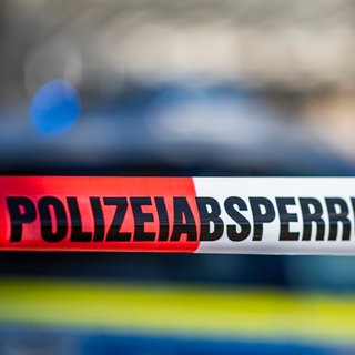 Ein Absperrband mit der Aufschrift «Polizeiabsperrung» ist vor einem Polizeiwagen aufgespannt.