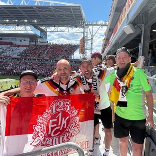 Vier Männer aus Dahn halten FCK-Fahne im Stadion beim WM Spiel Deutschland-Elfenbeinküste.