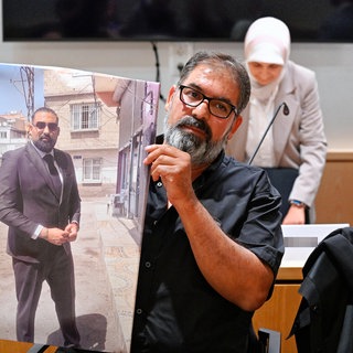 Erdal Calar, Vater des getöteten Zugbegleiters Serkan Calar, hält im Verhandlungssaal des Landgerichts ein Bild des Opfers in den Händen.