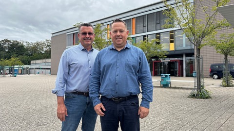 Eine Klasse ohne Smartphones: Schulleiter Markus Meier (links) und Elternbeirat Markus Siegrist (rechts) haben sich für das Pilotprojekt eingesetzt. (Zwei Männer stehen vor einem Schulgebäude.)