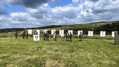 Menschen in Tarnuniform schießen am Truppenübungsplatz auf Zielscheiben. 