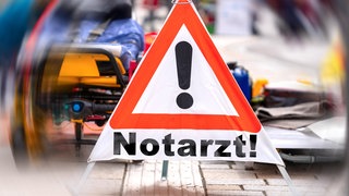 Die Fotomontage zeigt ein Warndreieck mit der Aufschrift "Notarzt" vor einer verschwommenen Rettungseinsatz: Bei einem Herz-Kreislauf-Stillstand dauert es im Bereich des Rettungsdienstbereichs Montabaur oft länger als vorgeschrieben, bis Hilfe kommt.