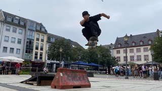 Ein junger Mann zeigt einen Trick mit einem Skateboard. Zu ihrem 25-jährigen Jubiläum durfte der Skateboardverein Koblenz noch einmal auf dem Koblenzer Münzplatz fahren.