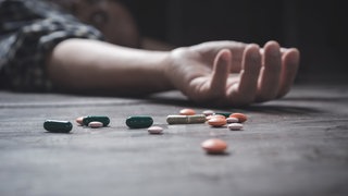 Ein Mann liegt auf dem Boden, daneben liegen Tabletten (Symbolbild)