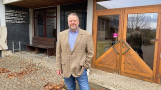 Ein Mann steht draußen vor der Tür eines Gebäudes. Claus Hensen aus dem Hunsrück hat die Jugendherberge in Sargenroth gekauft. Er will daraus ein Hostel machen.