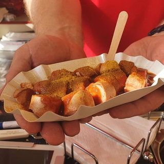 Eine Frau hält eine Currywurst in einer Schale in einem Imbisswagen.