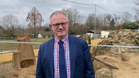 Oberbürgermeister Jan Einig steht am Gehege der Erdmännchen im Neuwieder Zoo